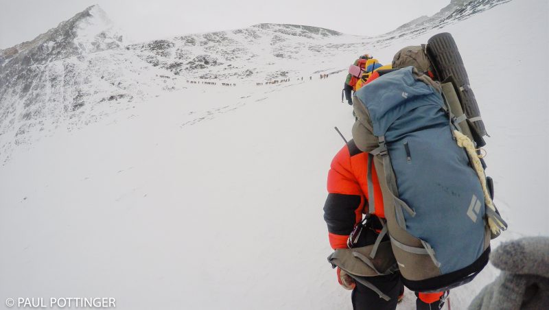 As we approach the next dogleg below the spur, a large traversing section, a column of descending climbers comes into focus. Some of our teammates are helping an ill climber at center of screen. (GoPro Screenshot)